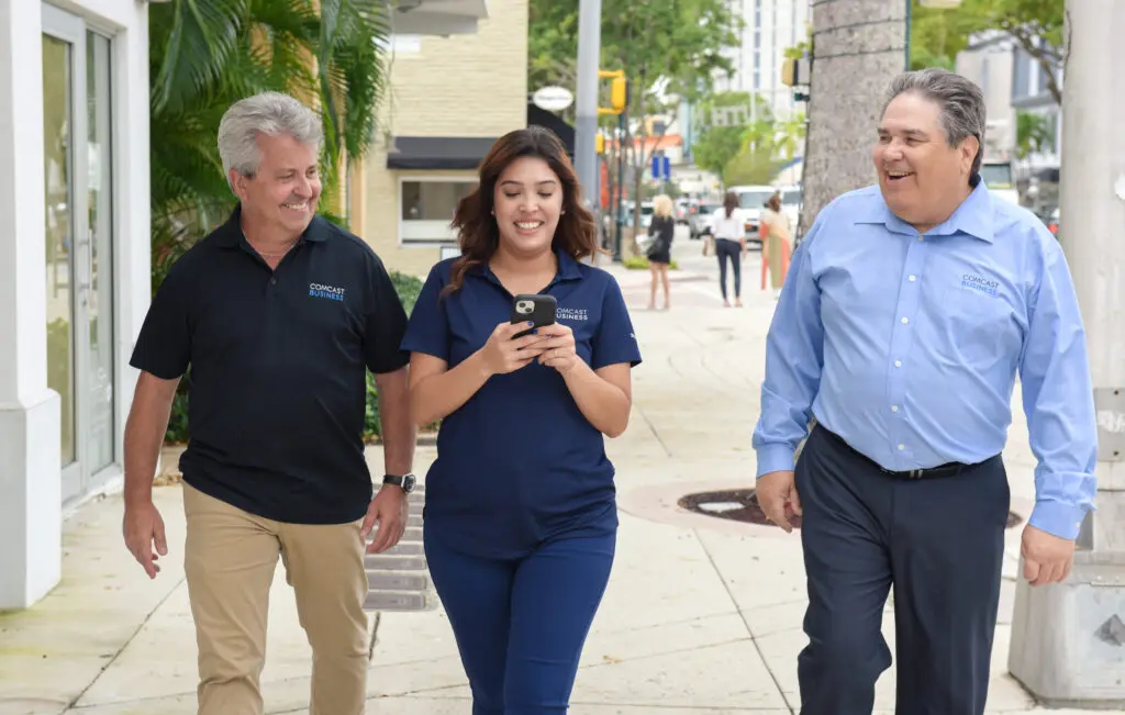 three people smiling and walking on a sidewalk