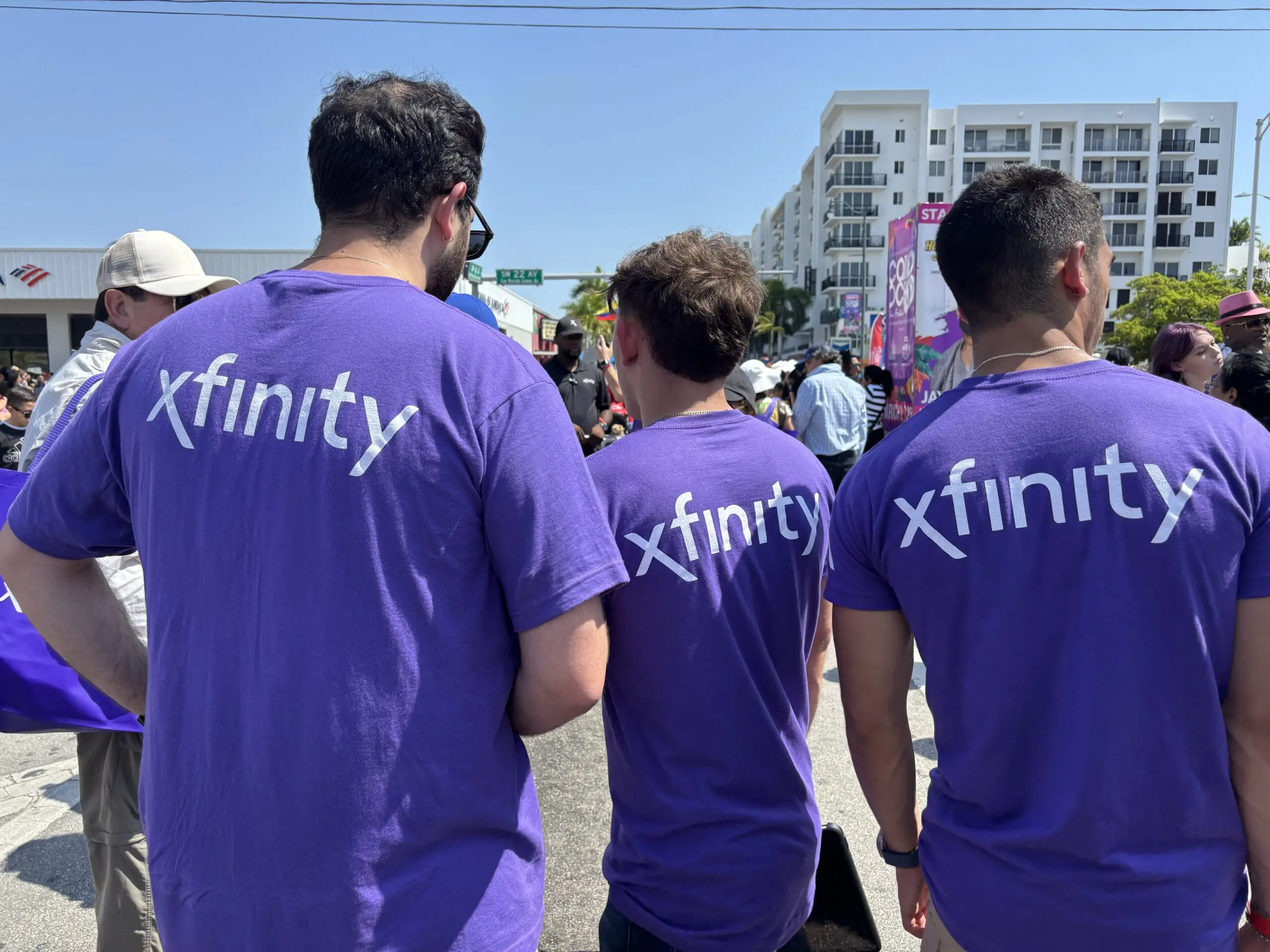 picture of the back of three men with an Xfinity logo on their shirts