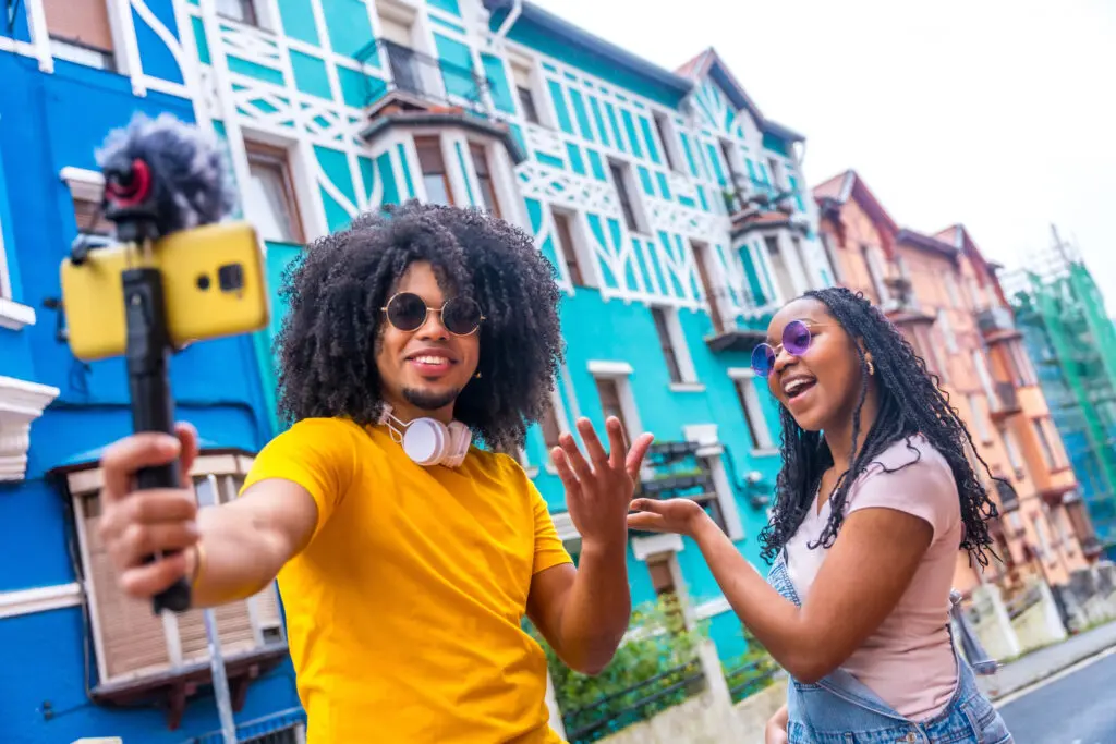 Xfinity Mobile customer in Florida utilizing new Premium Unlimited plans 4K streaming and hotspot data on WiFi. Influencers recording an online video using phone and mic while visiting a colorful street