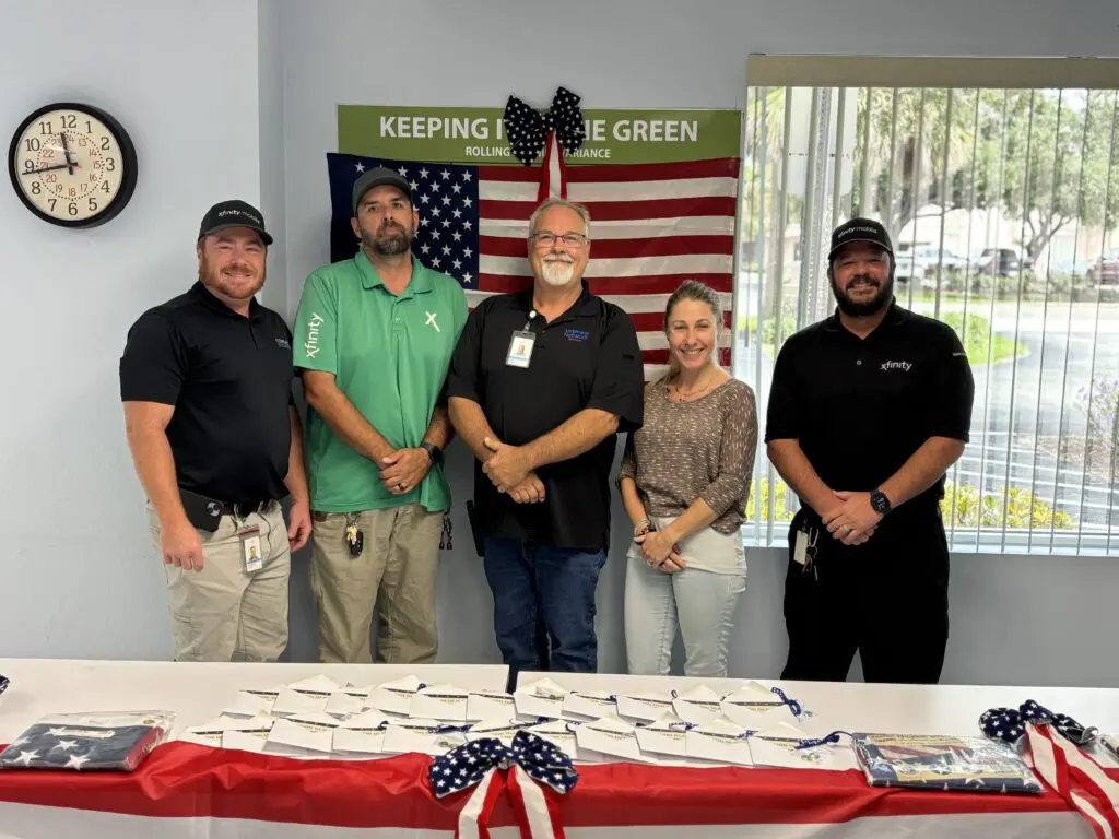 Four men and a woman pose for a picture with the American flag in the background.