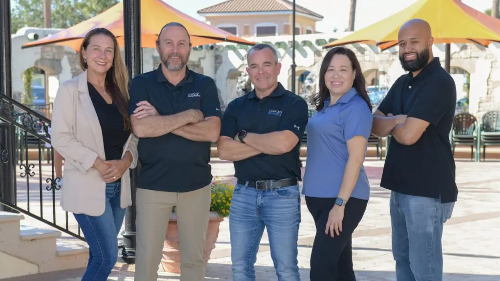 A group of Comcast Business employees posing together outdoors, wearing branded shirts and smiling for the camera.