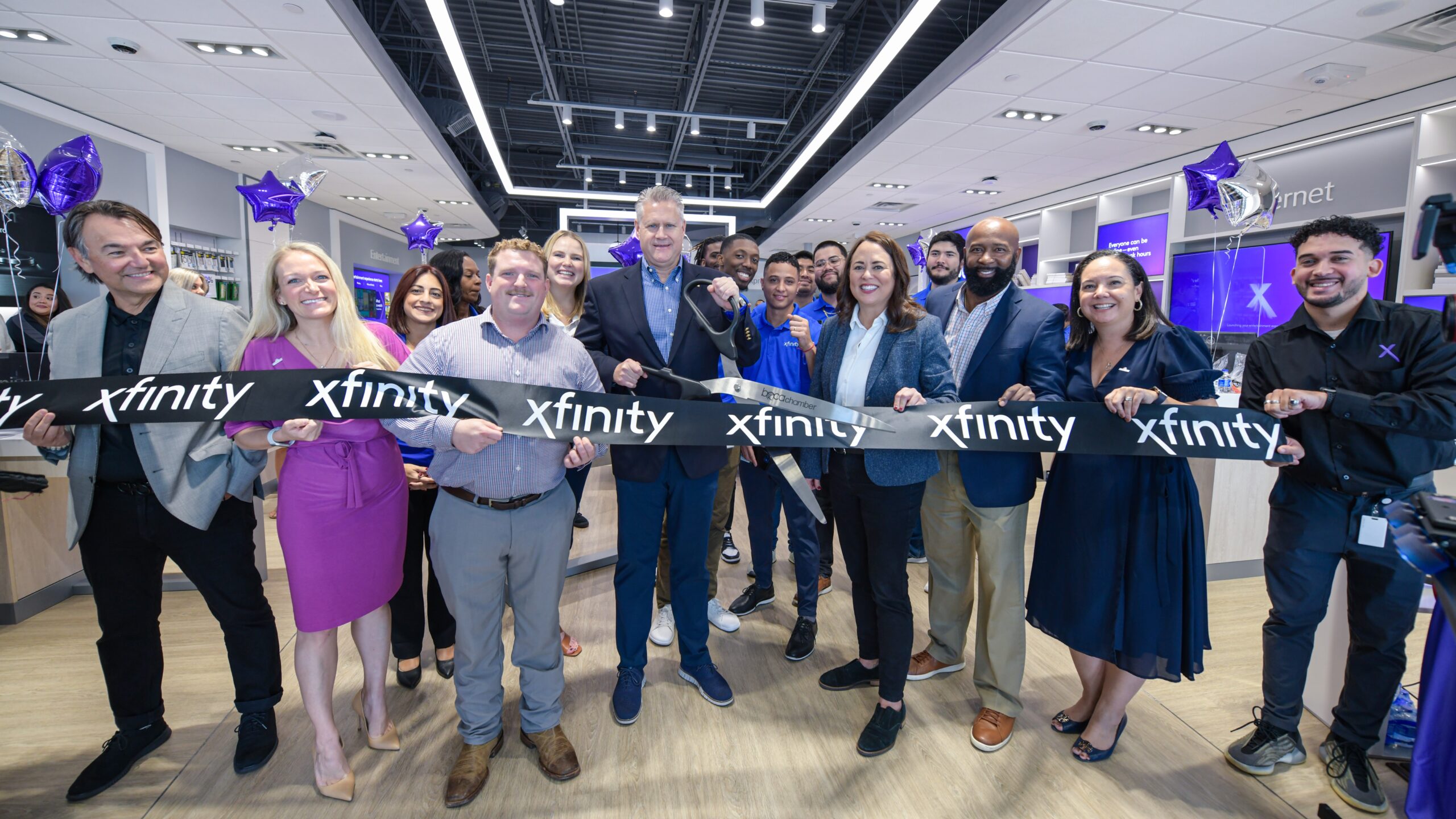 Xfinity Story team members, customers, government officials, and community partners standing in a line holding a large Xfinity branded ribbon at the store opening ceremony.