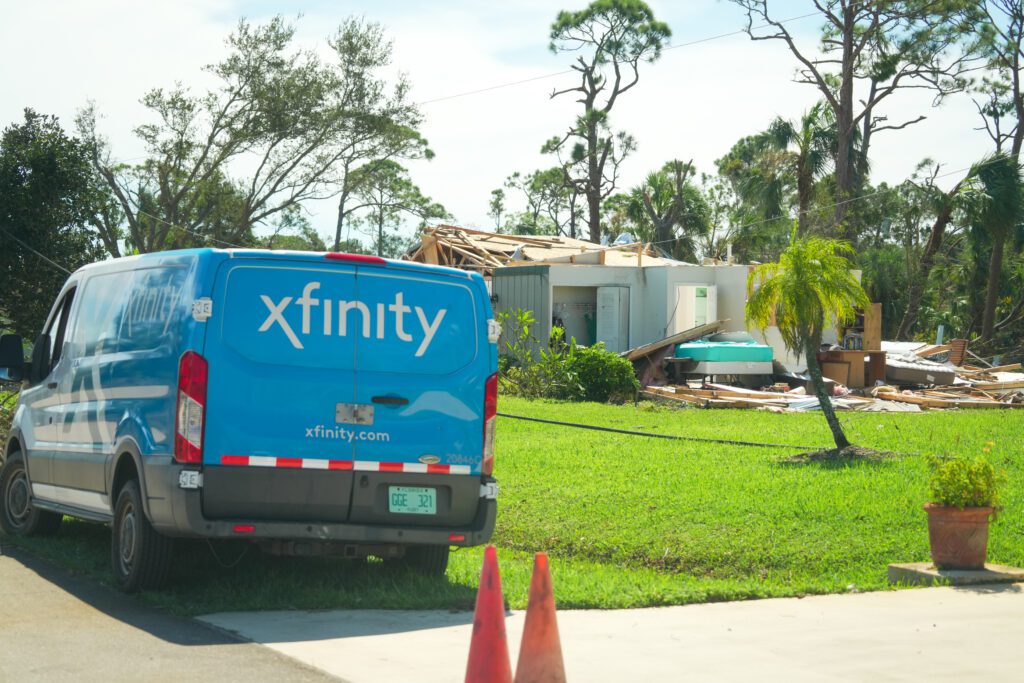 Comcast van is parked in a driveway outside a home damaged by a storm