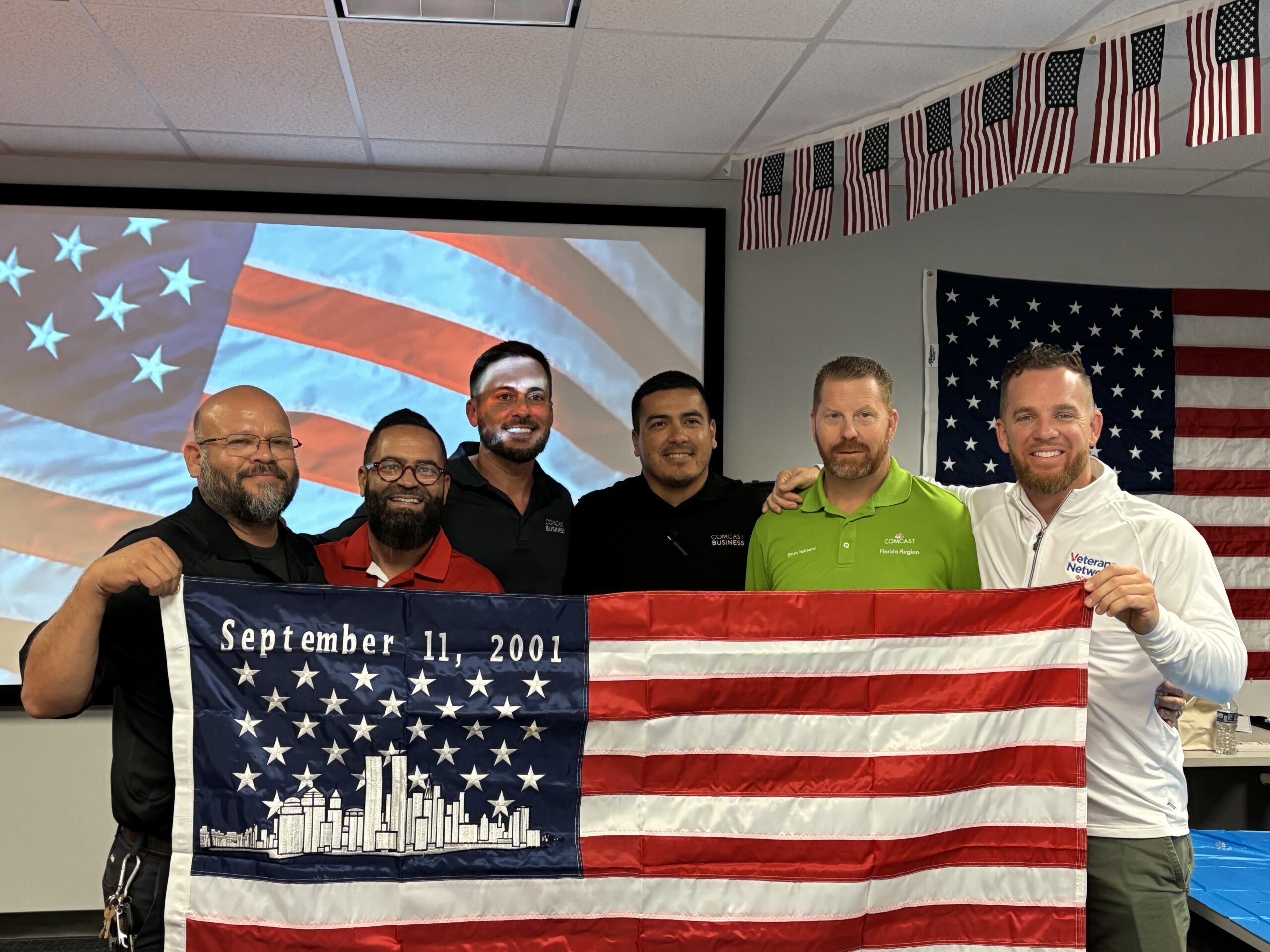 Six men posing with an Amercian flag in hand.