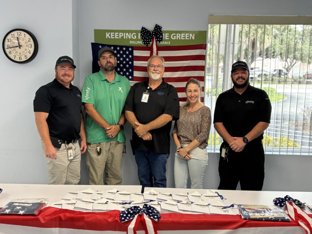 Four men and a woman pose for a picture with the American flag in the background.