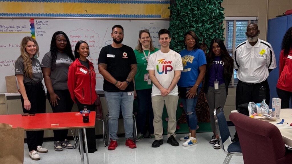 A group of Comcast volunteers in Team UP shirts smiling together inside Jacksonville Heights Elementary during the City Year House Day event.