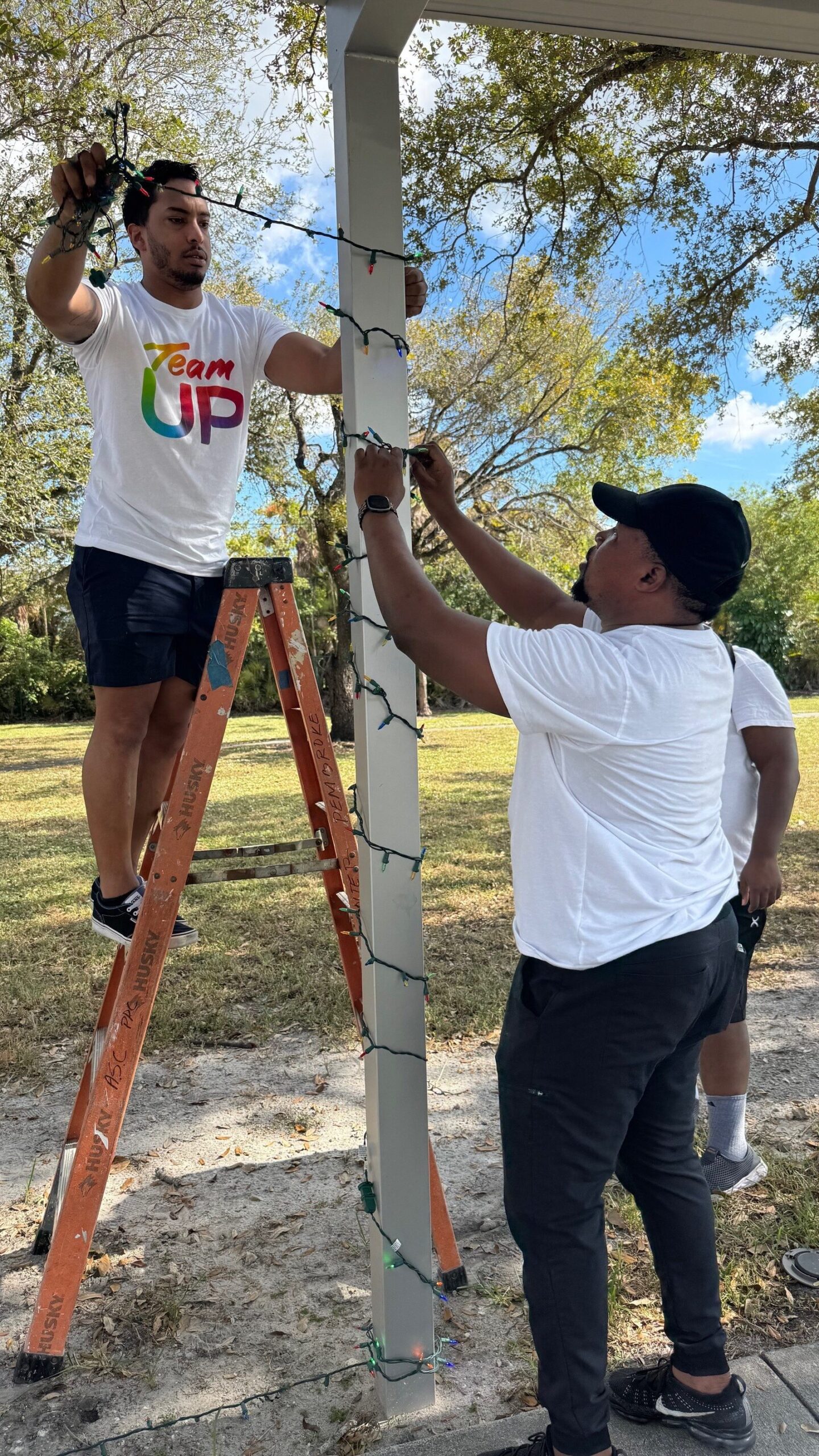 Volunteers string lights around a pole.