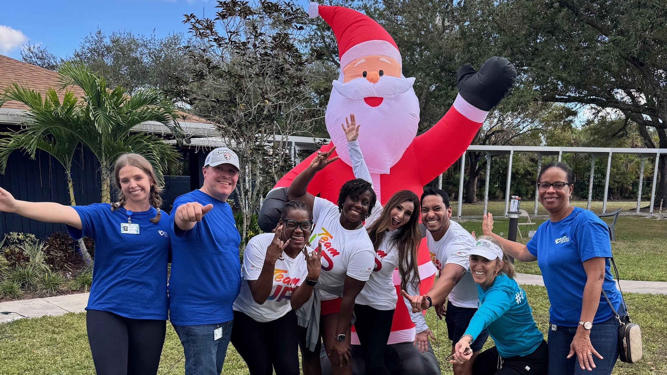 A group of Comcast employees poses with an inflatable Santa Claus decoration.