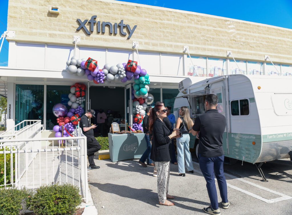 Exterior view of the Xfinity store with a balloon arch at the entrance, a food truck parked nearby, and people mingling outside.