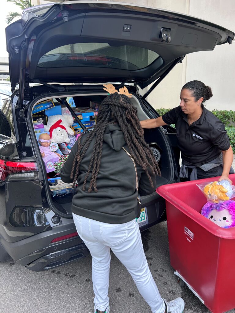 Two women load toys into the back of a car.
